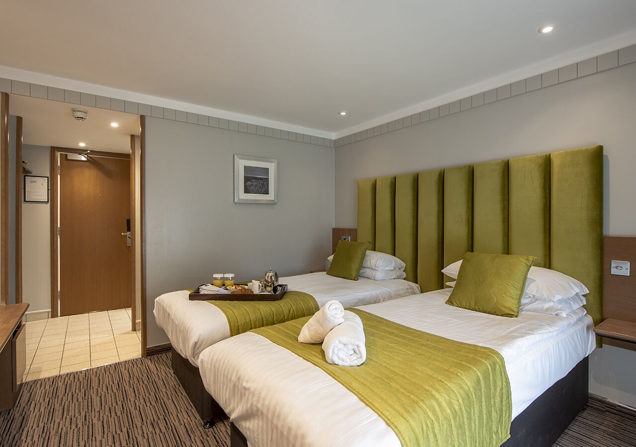 Habitación de hotel con dos camas, una puerta de madera, un cuadro enmarcado en la pared y una mesita con una bandeja de alimentos para el desayuno.