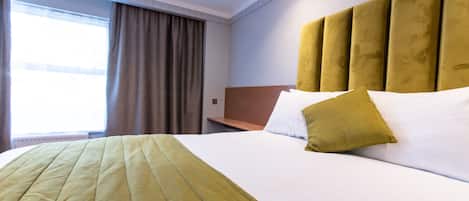 A hotel room with a large bed, a headboard, and a window with curtains.