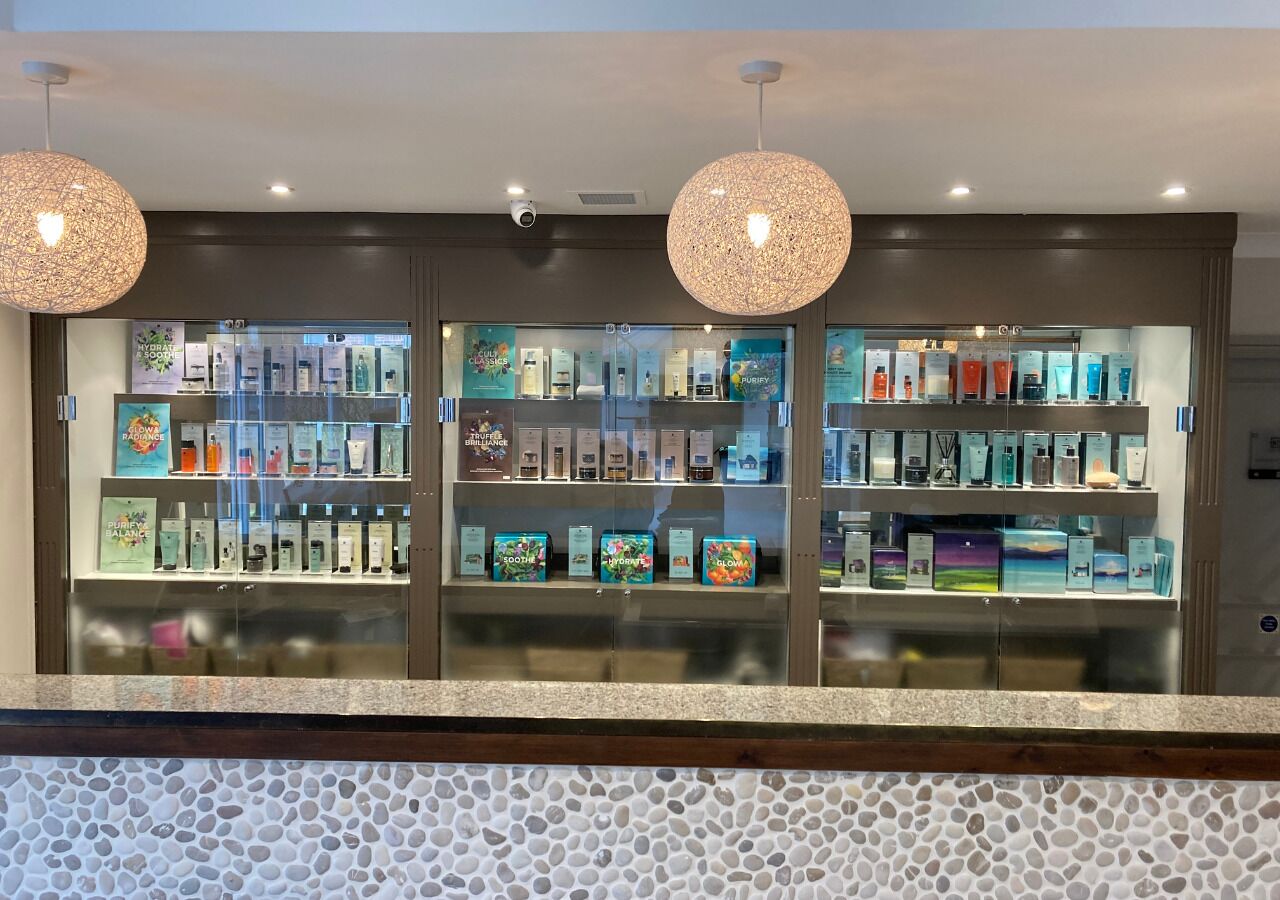 A reception area with a glass display of various products, a patterned wall, and two spherical hanging lights.