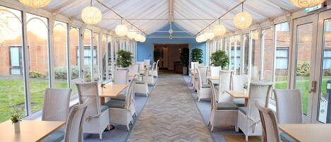 A covered dining area with wicker furniture, large windows, and a herringbone floor pattern.