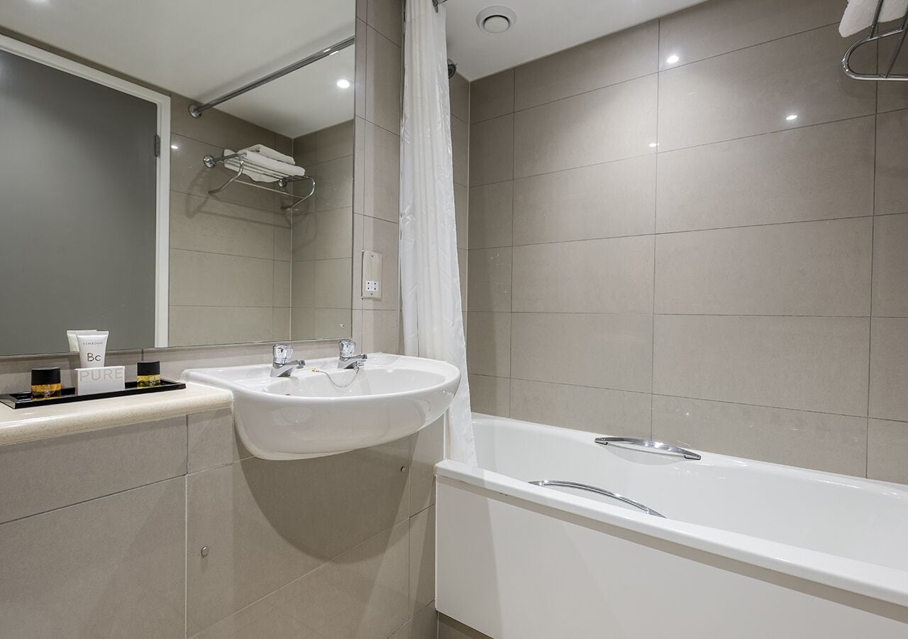 A modern bathroom with a sink, mirror, and bathtub.