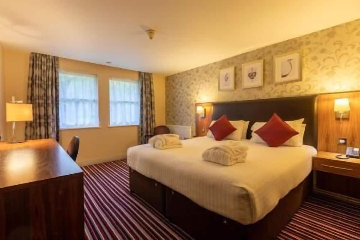 A hotel room with a large bed, two bedside tables, a desk, and a chair.