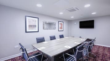 Un salón de conferencias con una mesa larga, seis sillas, un reloj y cuadros en las paredes.
