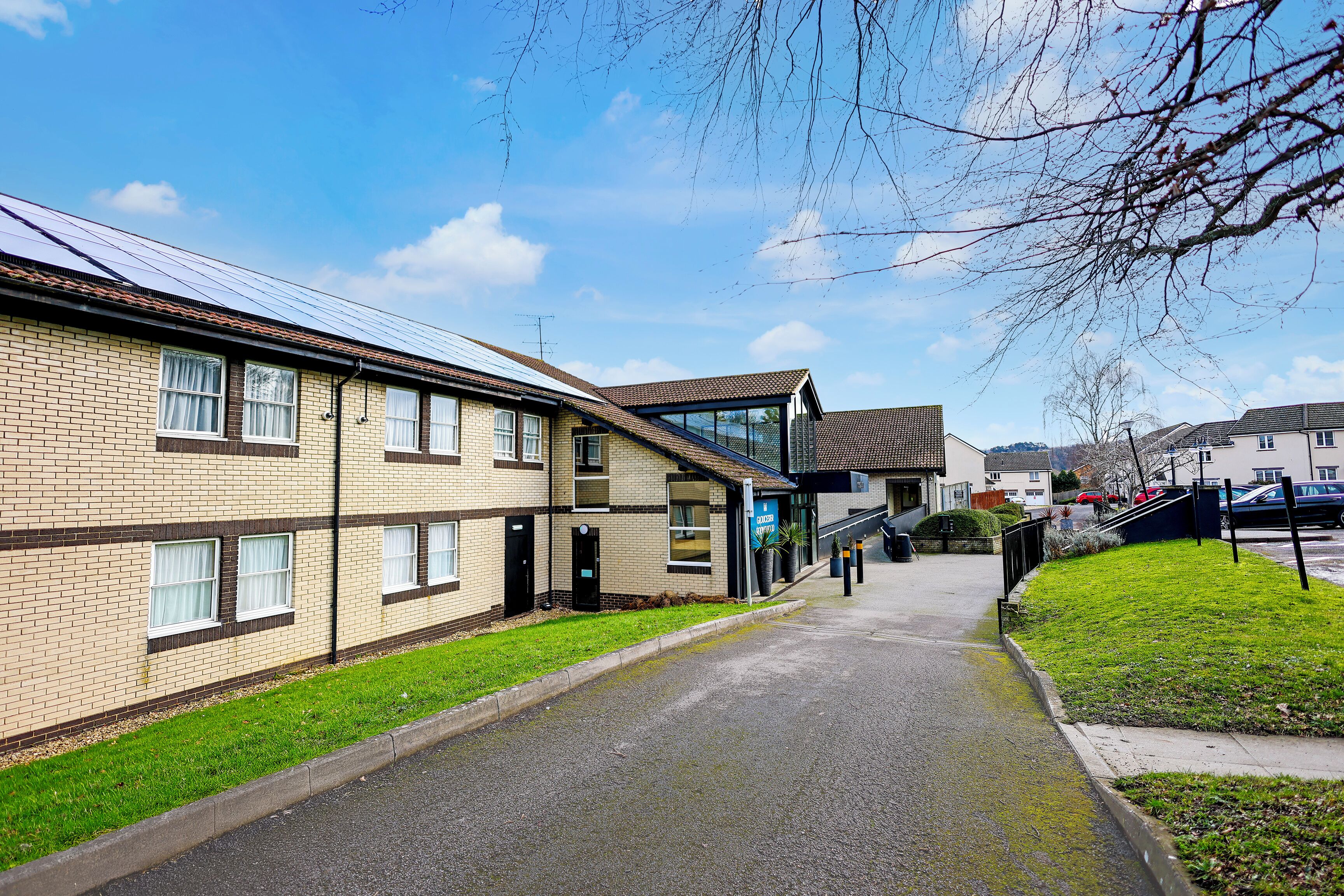 A multi-story building with a brick facade, a covered walkway, and a green lawn.