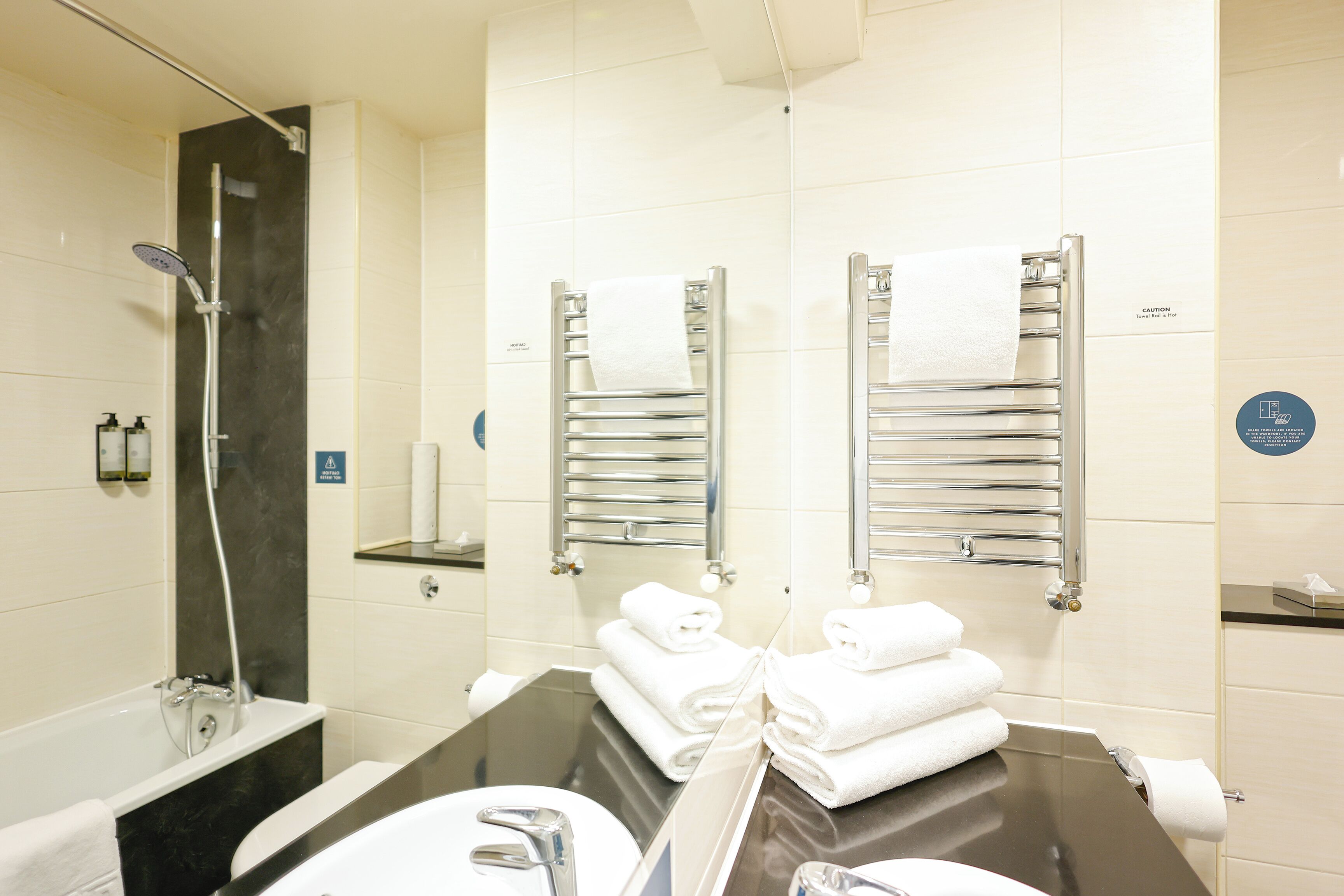 Un baño moderno con ducha de vidrio, encimera negra y dos toalleros con toallas dobladas.