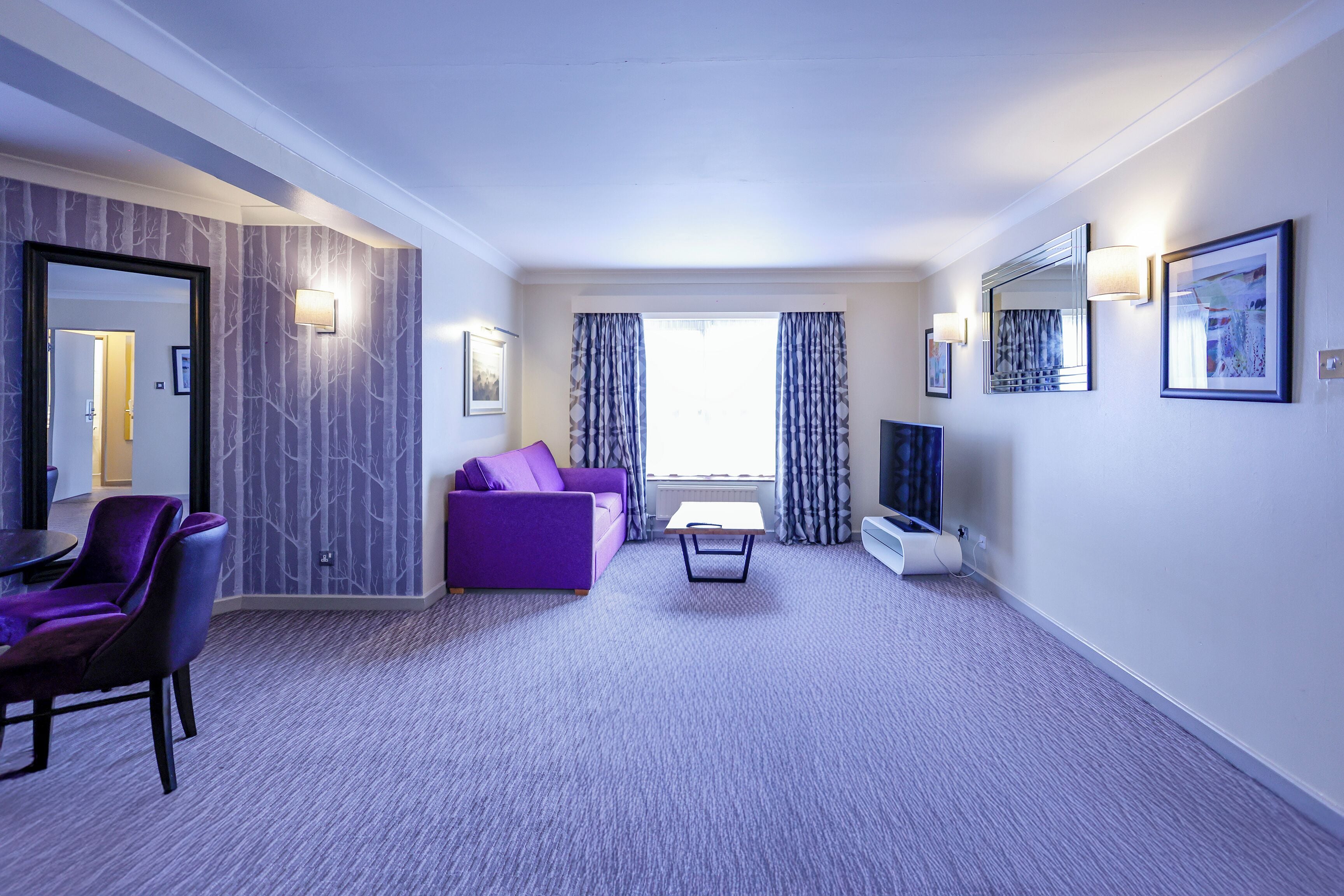 A modern hotel room with a purple sofa, a small table, and a TV.