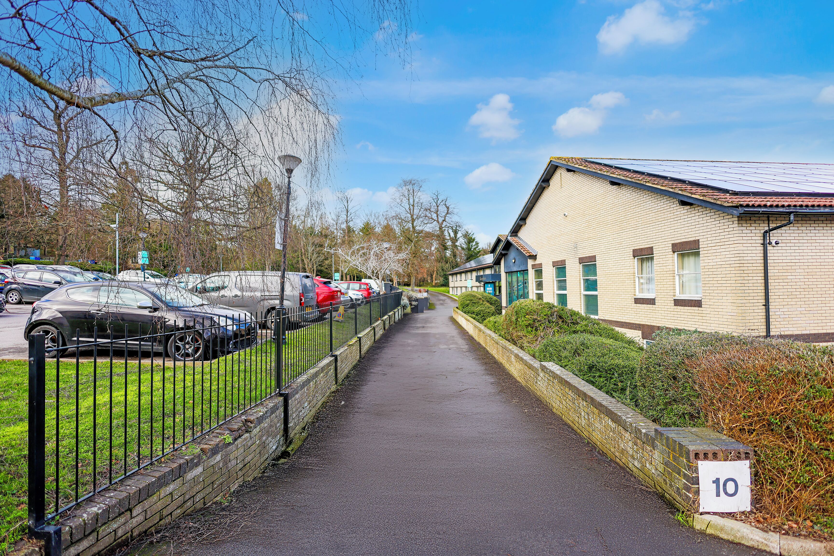 A paved pathway leading to a building with a number 10 sign, surrounded by parked cars and a fence.