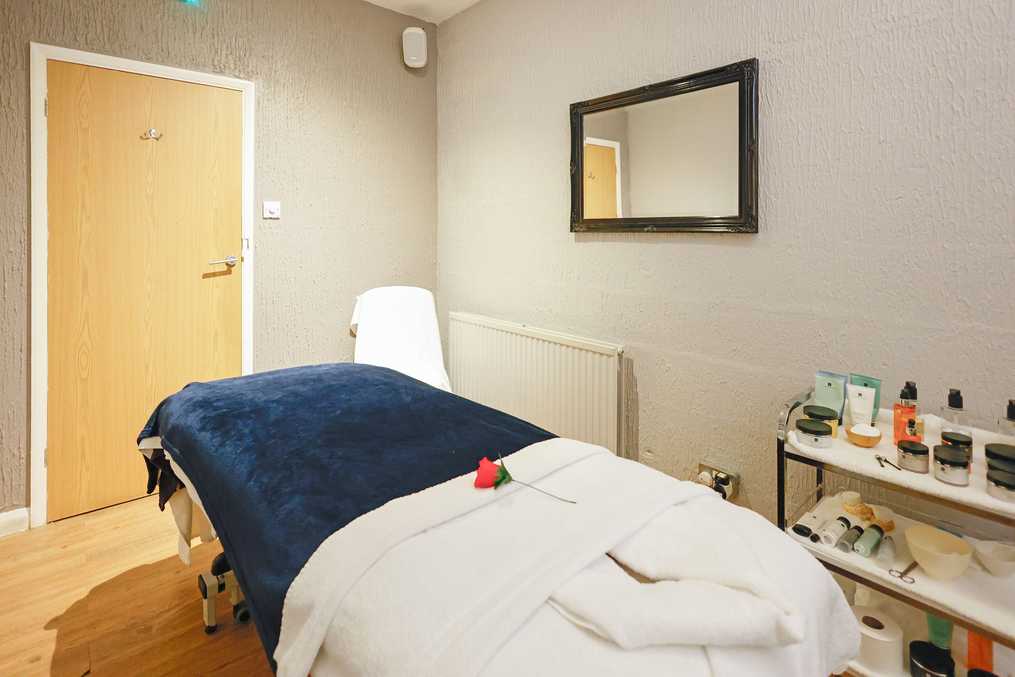 A room with a bed, a white chair, a shelf with toiletries, and a wooden door.