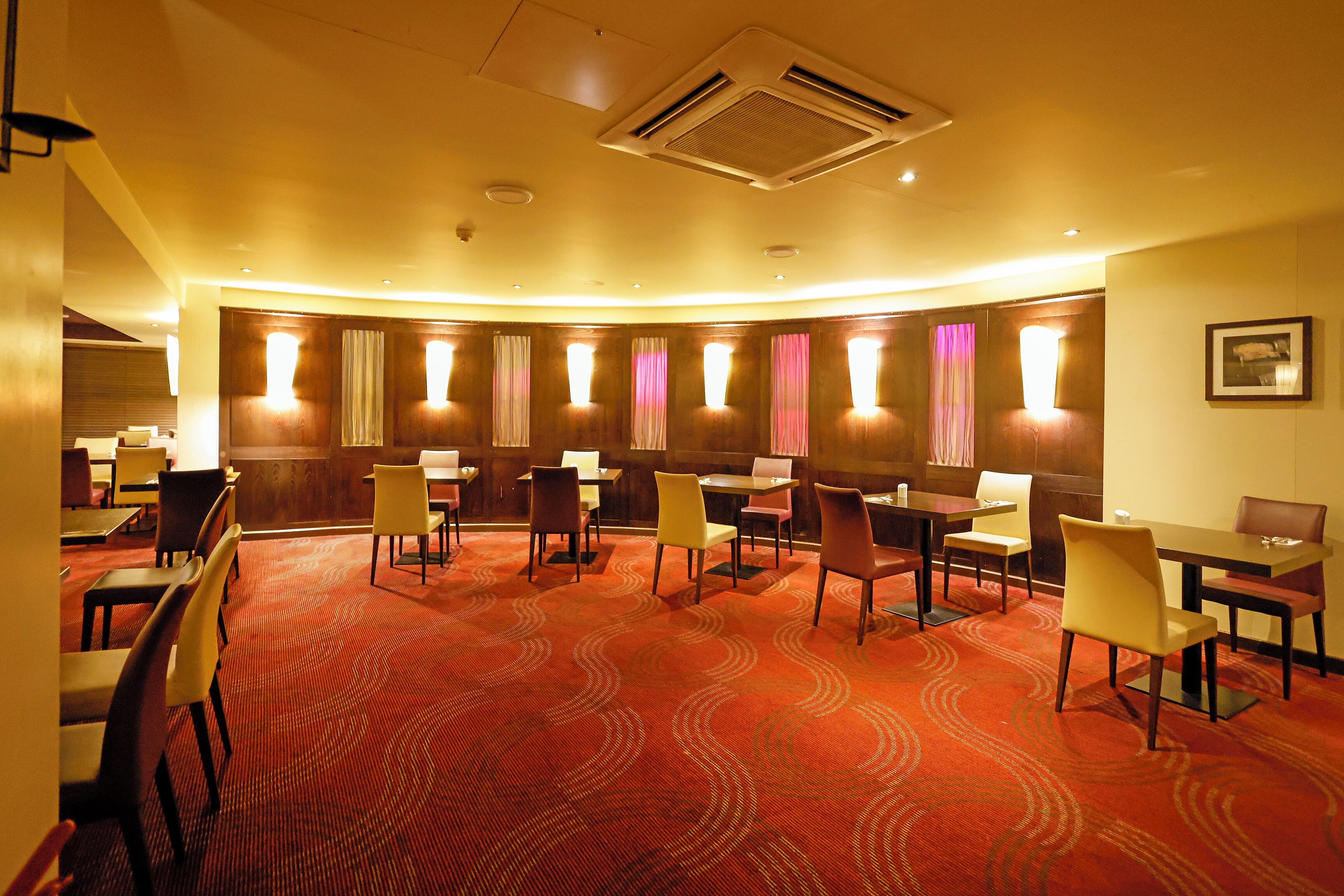 A hotel room with a red carpet, multiple tables and chairs, and a large window with curtains.