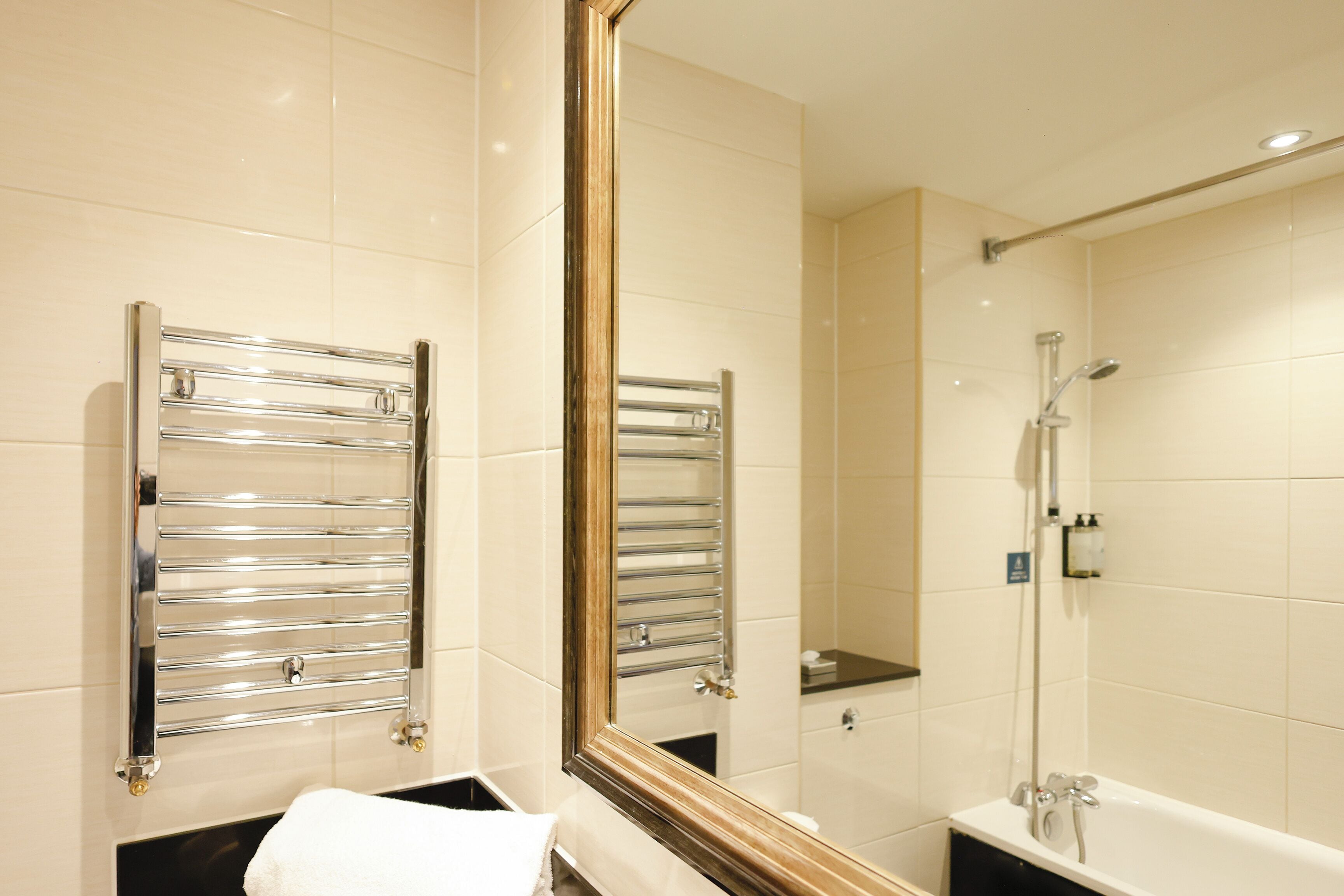 A modern bathroom with a large mirror, chrome towel racks, a bathtub, and a shower.