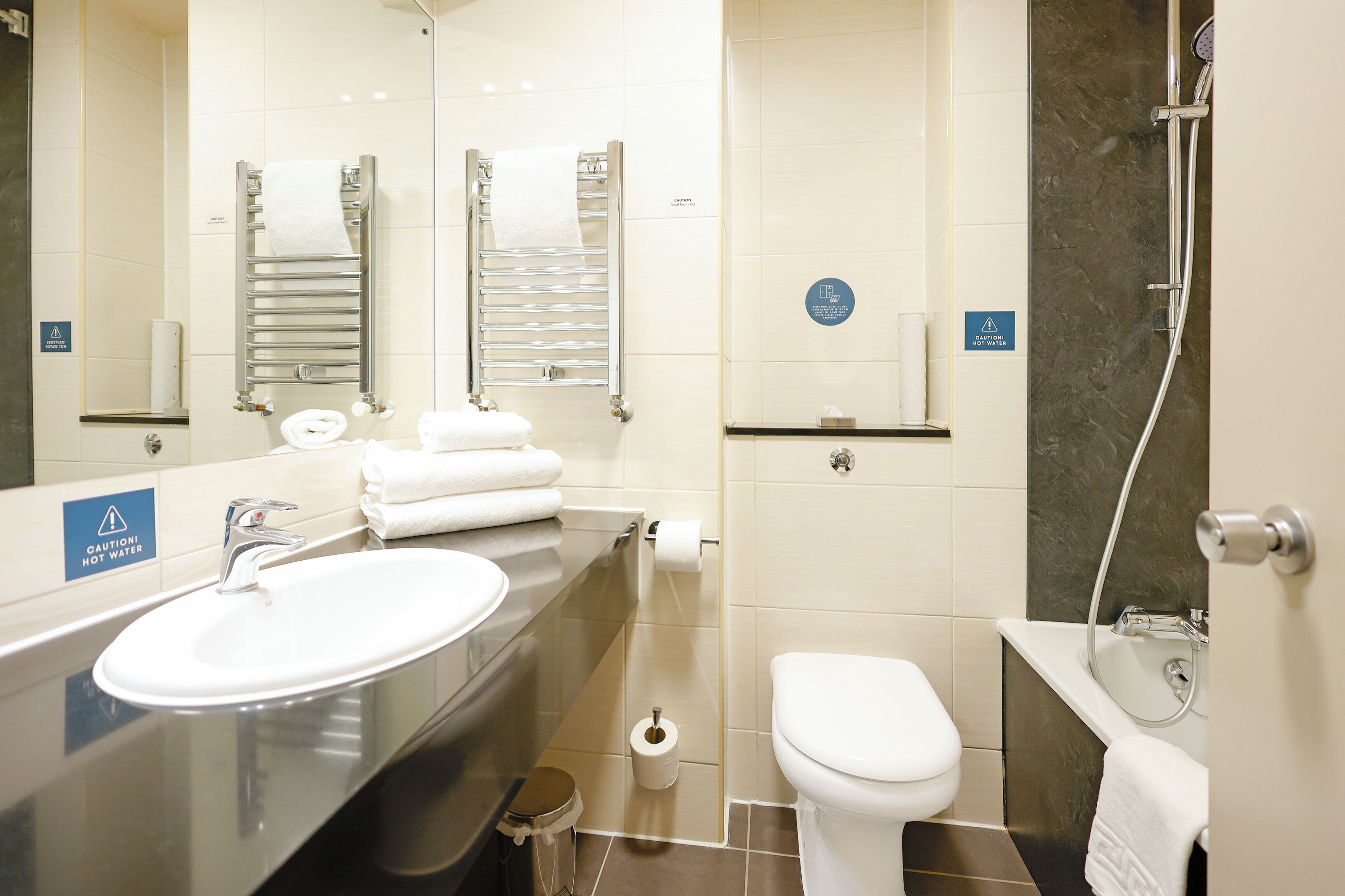 Een moderne badkamer met een wastafel, toilet en douche. Handdoeken en een toiletrol zijn zichtbaar.