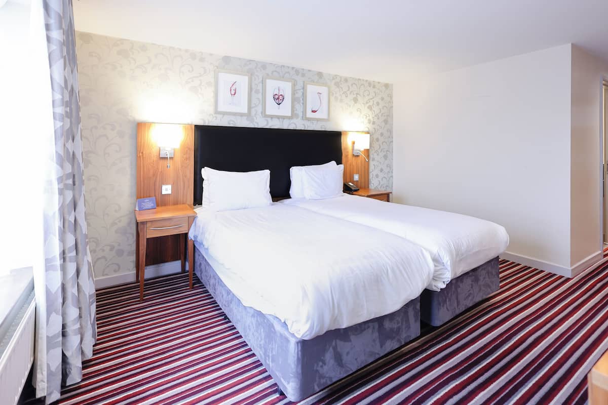 A hotel room with a large bed, two bedside tables, a nightstand, a shower area, and a curtain.