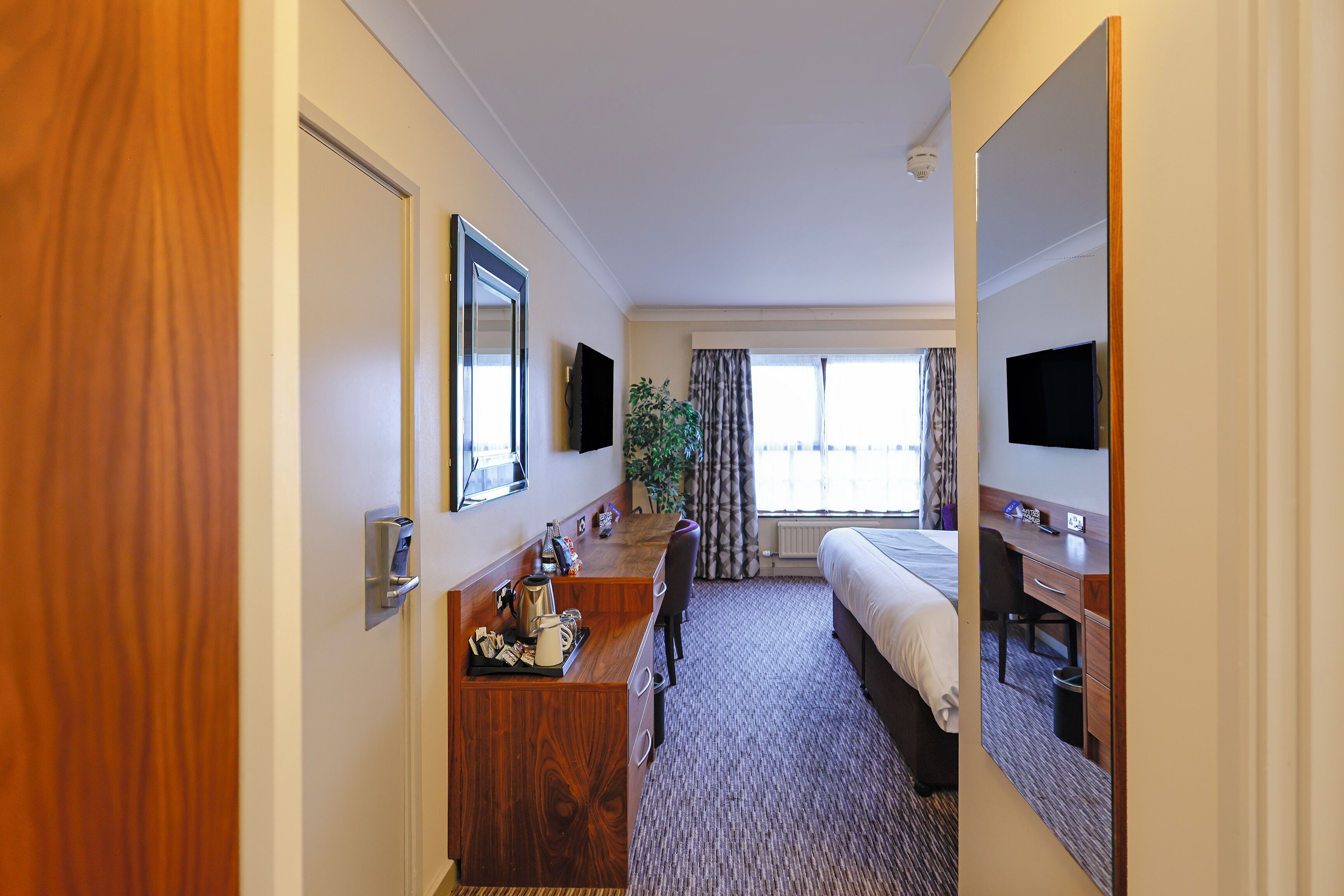 Ein Hotelzimmer mit einem Bett, einem Schreibtisch mit Stuhl, einem Fernseher und einem Vorhangfenster.