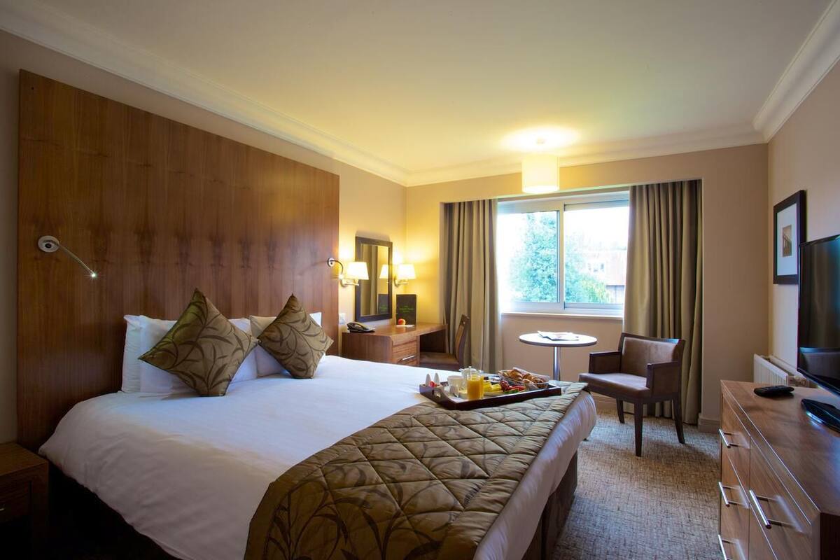 Una habitación de hotel con una cama grande, un escritorio con lámpara, una silla, un televisor y una ventana con cortinas.