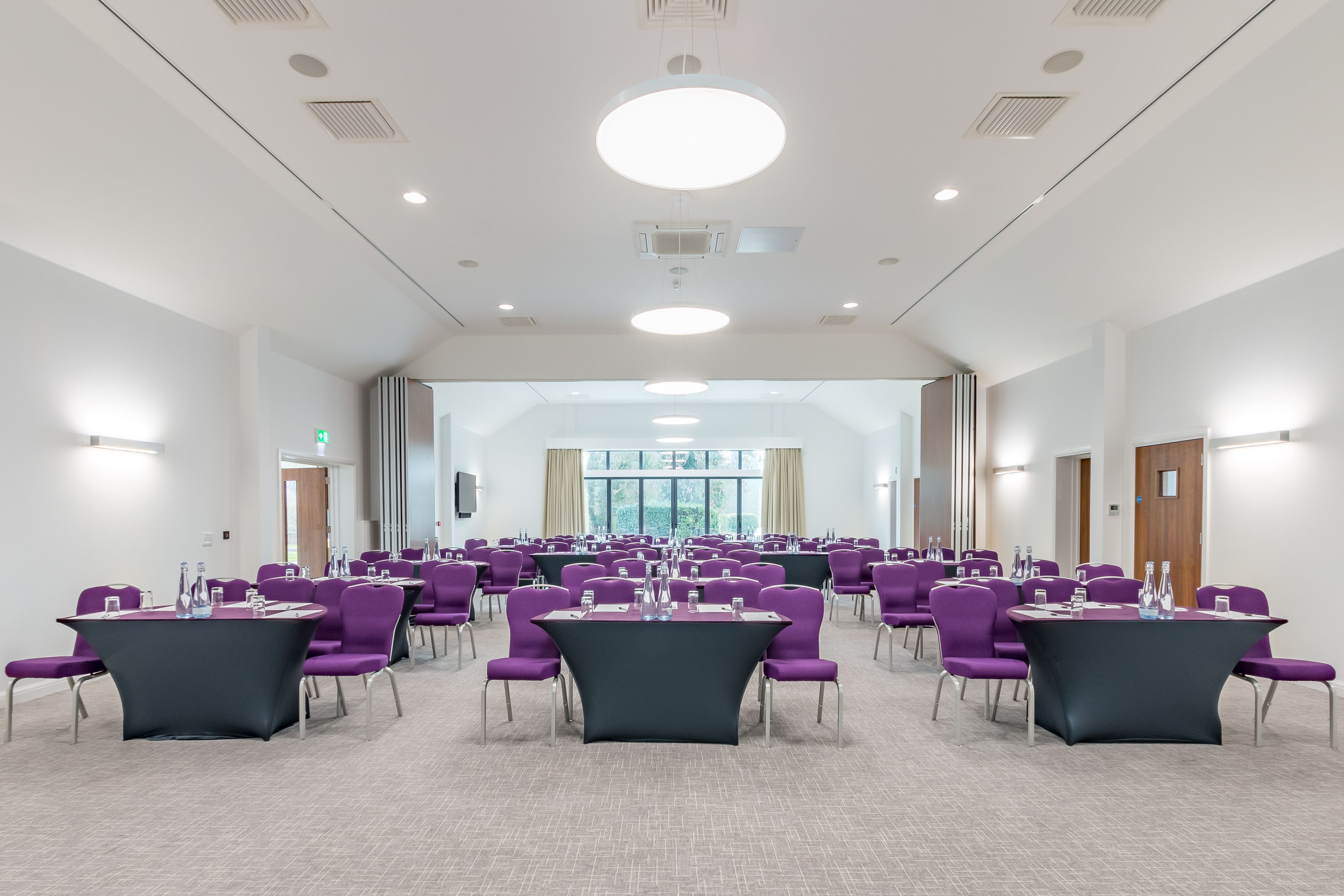 A conference room with multiple tables and chairs, large windows, and a modern ceiling design.