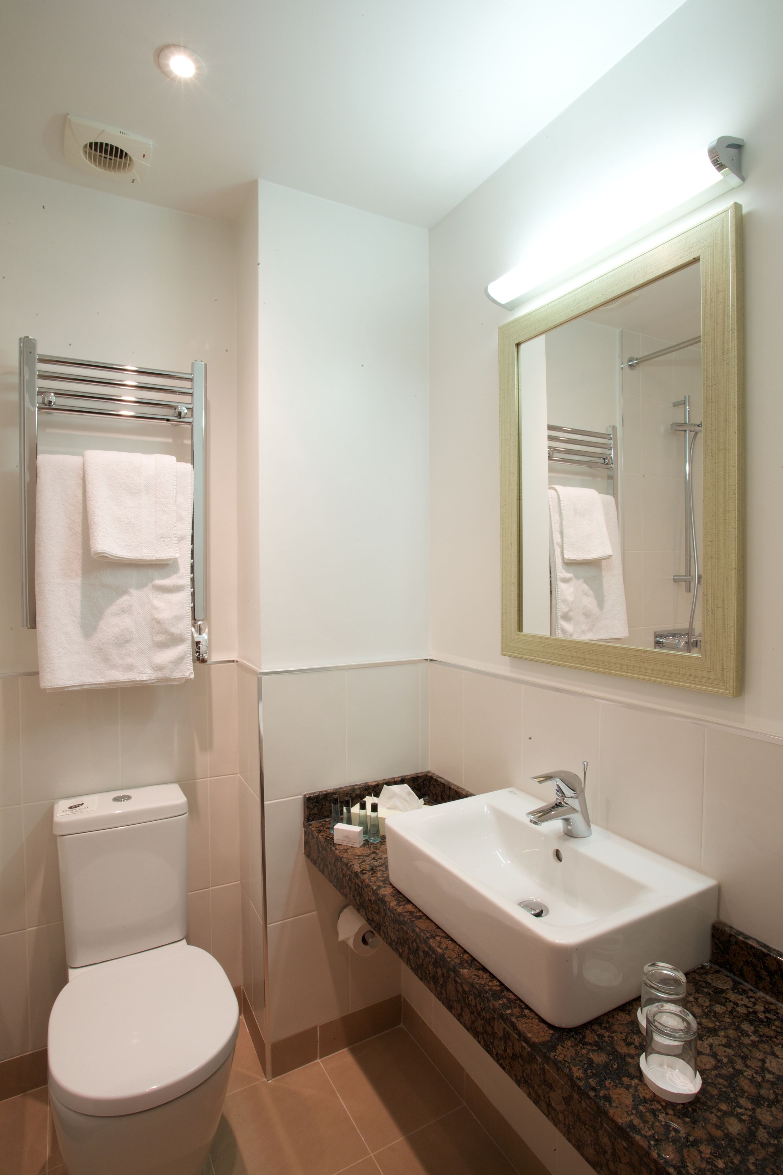 A bathroom with a white toilet, a sink with a mirror above it, and a towel rack with white towels.