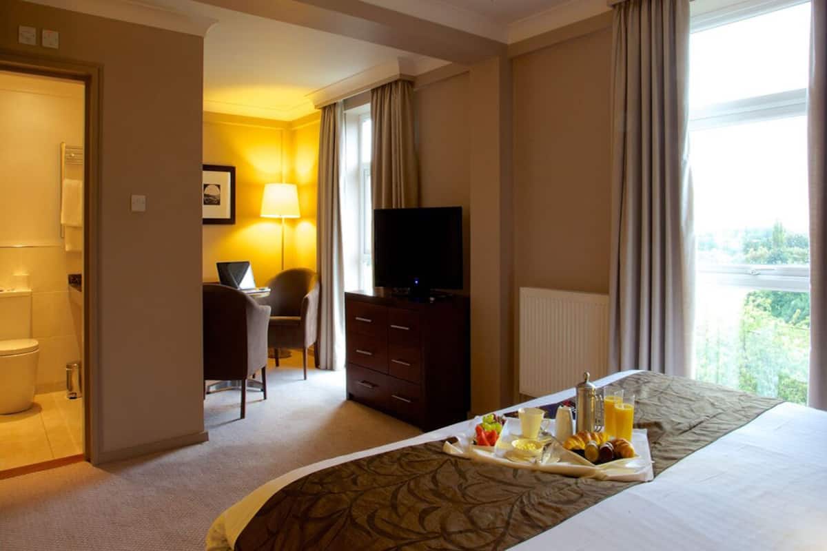 Una habitación de hotel con cama, escritorio, televisor y bandeja para el desayuno.