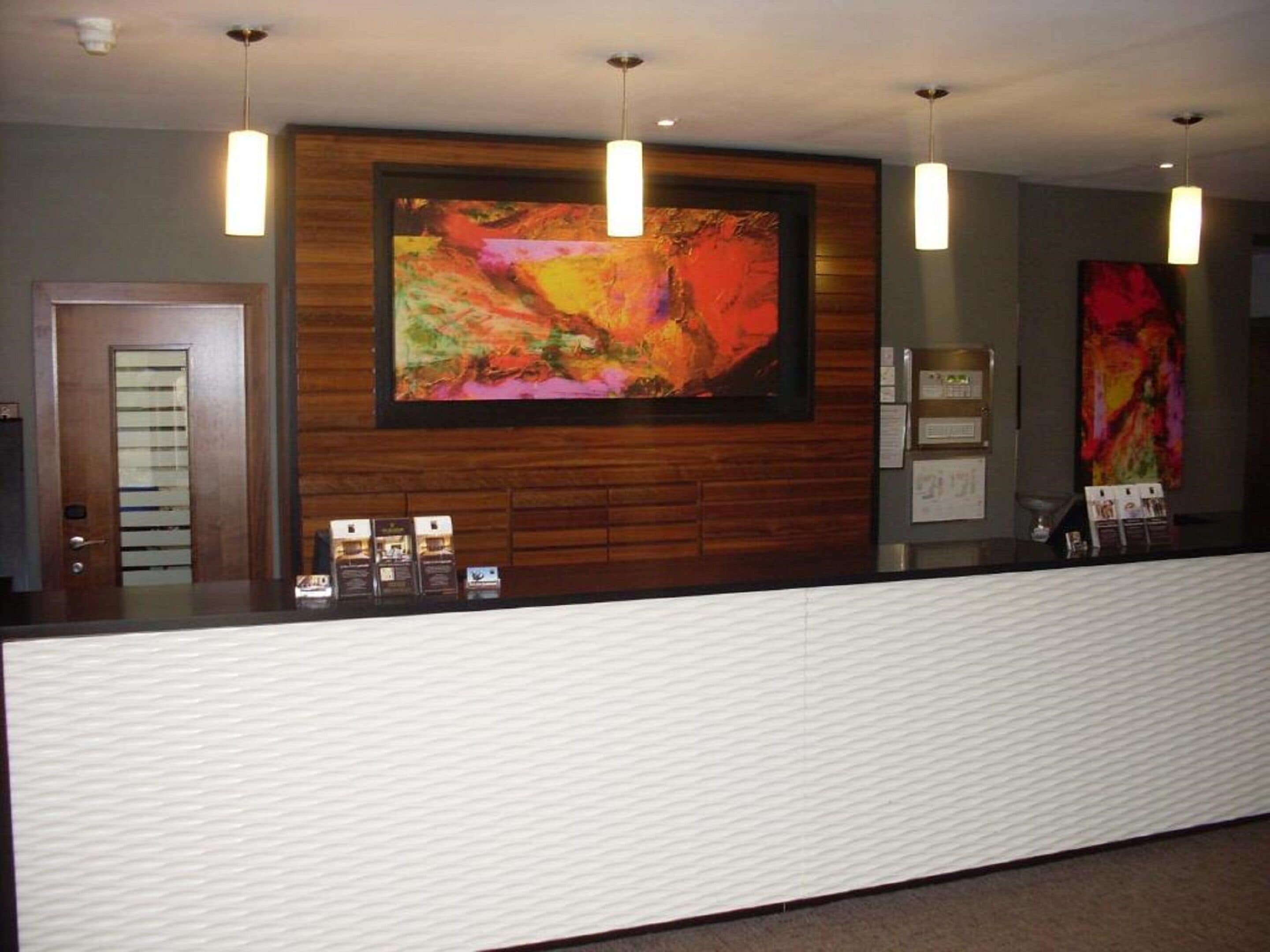 A reception area with a wooden reception desk, a large abstract painting above it, and three pendant lights.