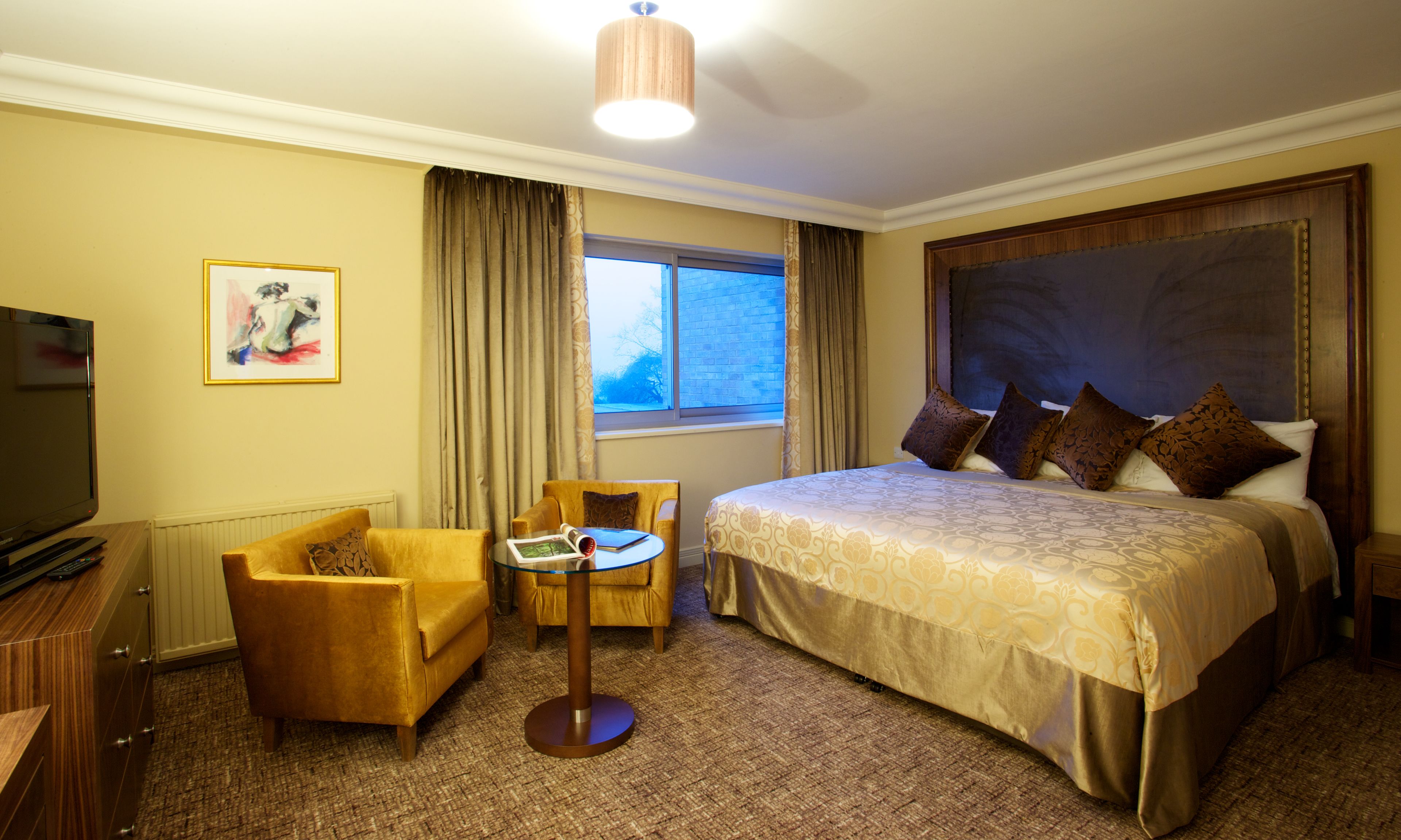 A hotel room with a large bed, a desk with a chair, a television, and a window with curtains.