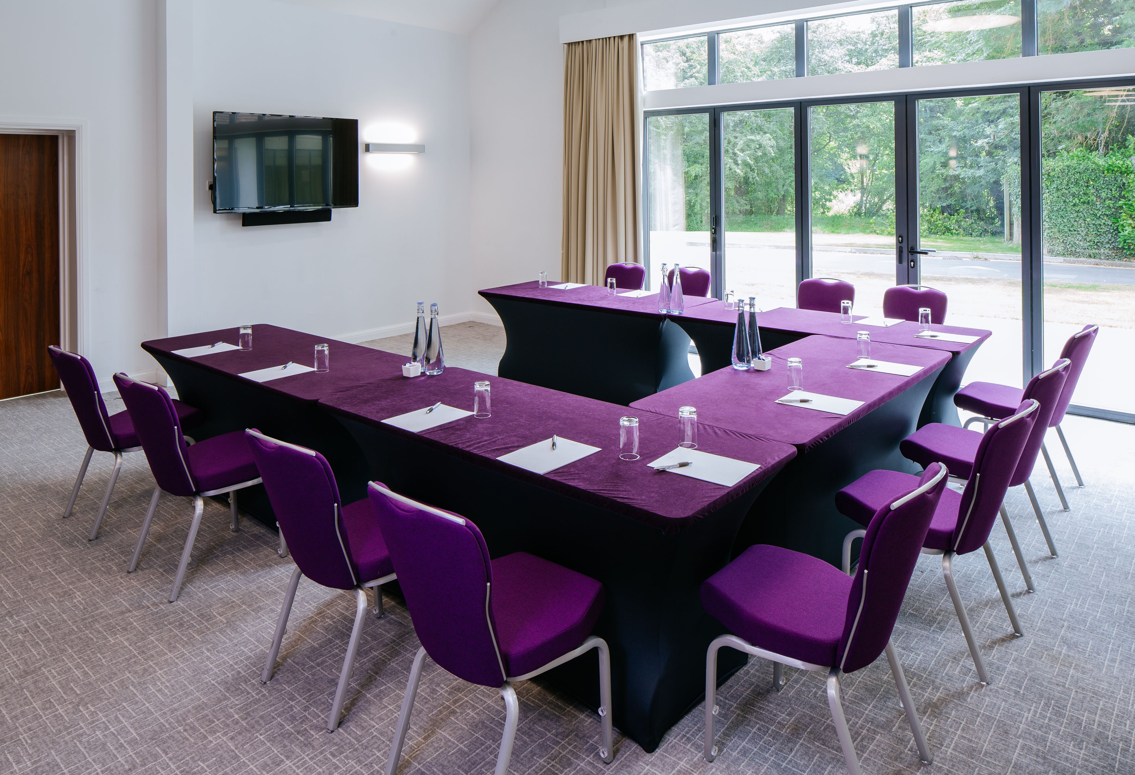 A conference room with a long table, purple chairs, and a flat-screen TV on the wall.