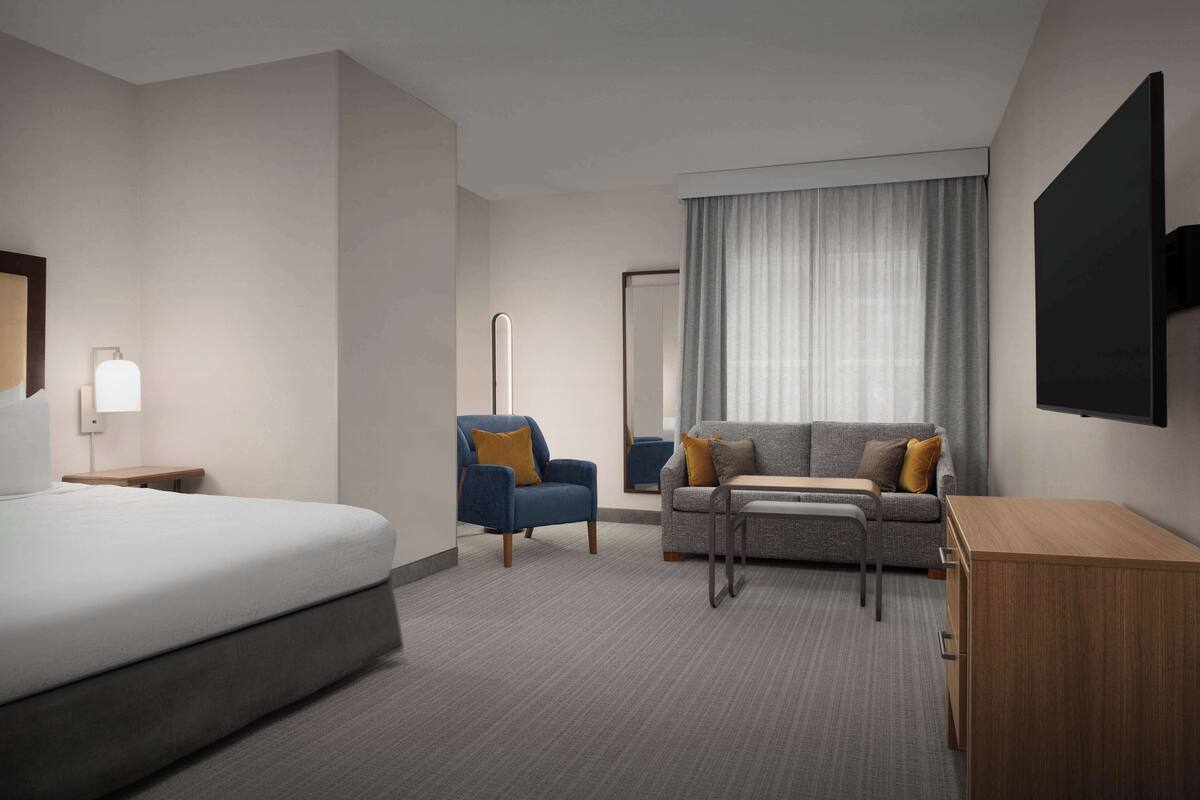 Una habitación de hotel moderna con una cama grande, un sofá, una silla, un escritorio y un televisor montado en la pared.