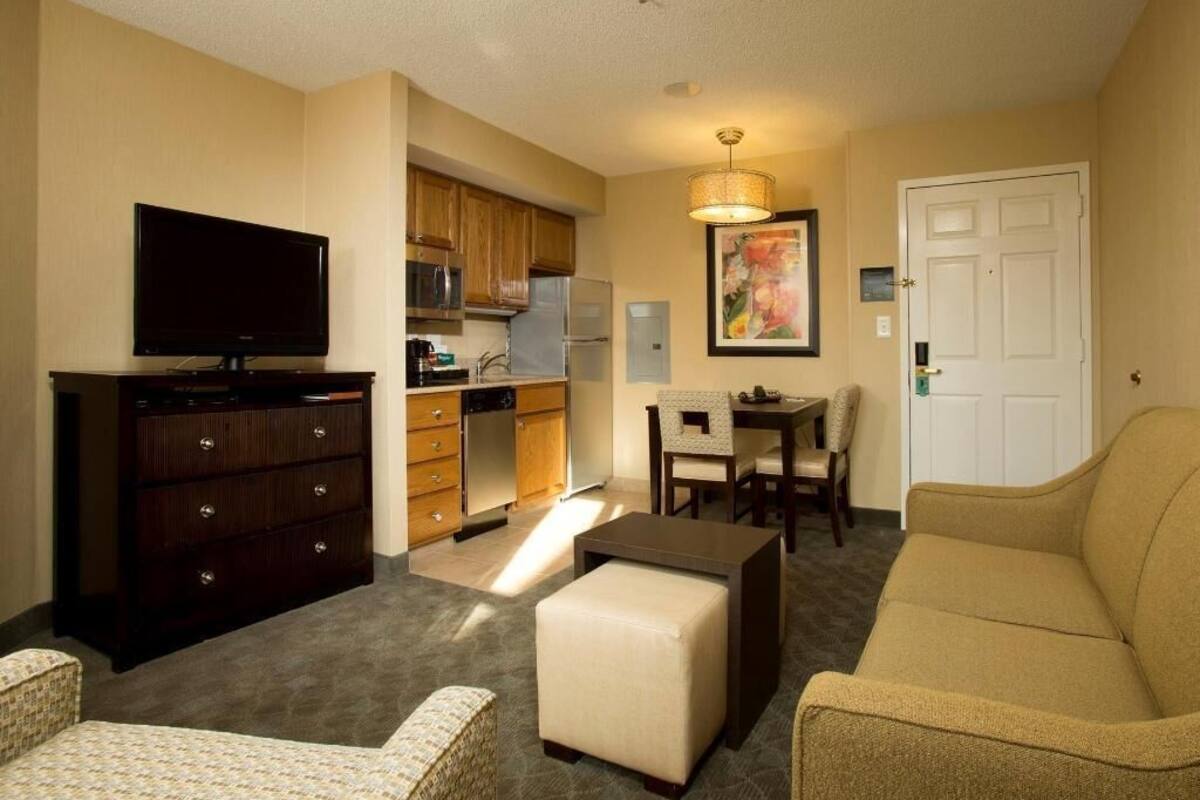 Una sala de estar con televisor, sofá, reposapiés y una zona de comedor con sillas y mesa.