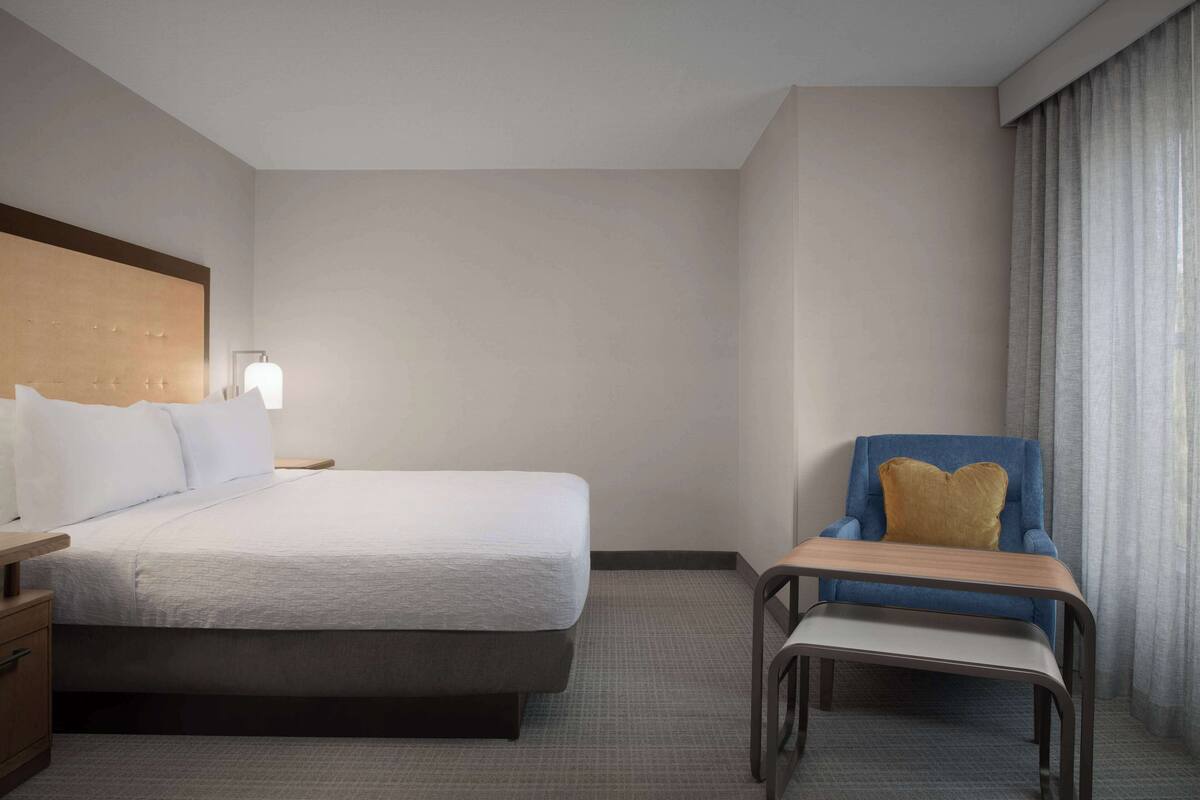 Una habitación de hotel con cama, una silla, una mesita de noche y una lámpara.