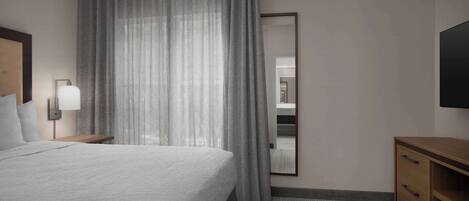 A hotel room with a large bed, a bedside table with a lamp, a wooden dresser, and a large mirror on the wall.