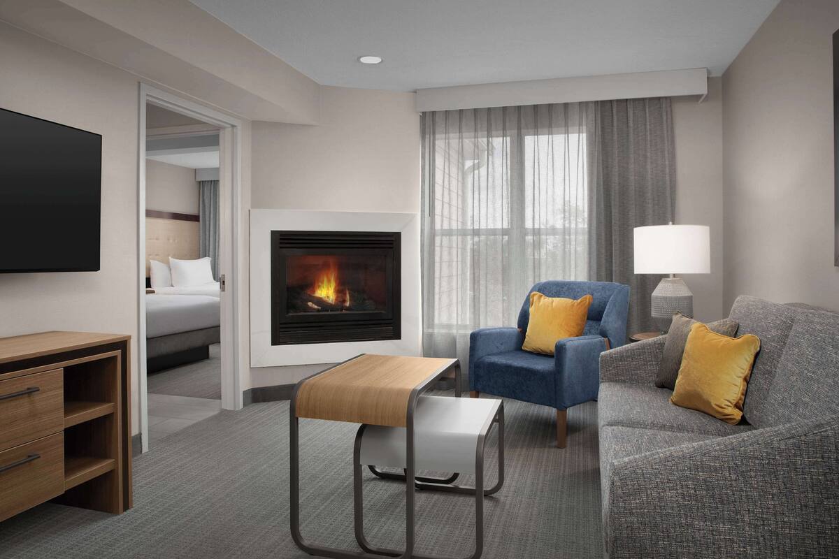 Una habitación de hotel moderna con chimenea, un sofá, una silla, un televisor y un escritorio.