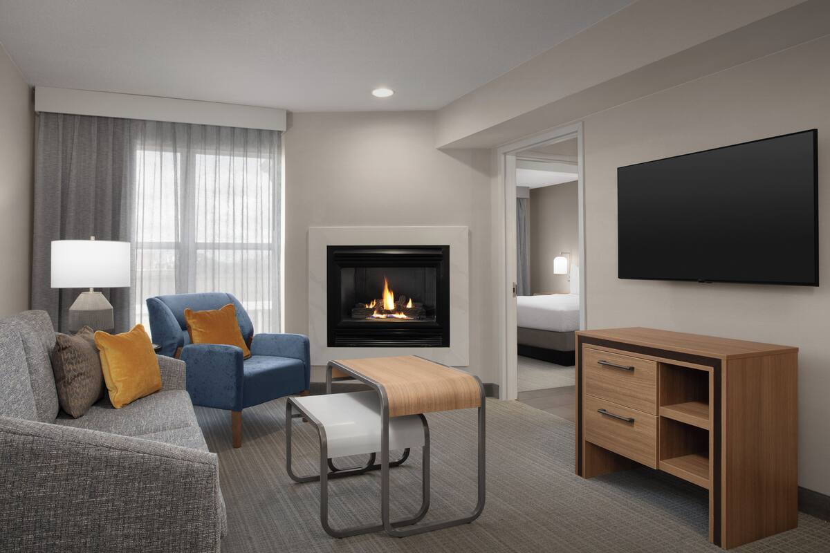 Habitación de hotel con sofá, sillón, mesita de noche, televisor y chimenea.