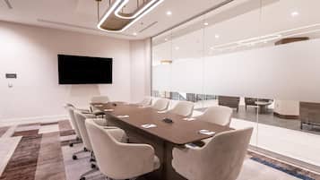 A conference room with a long table, white chairs, a flat-screen TV, and a glass wall.