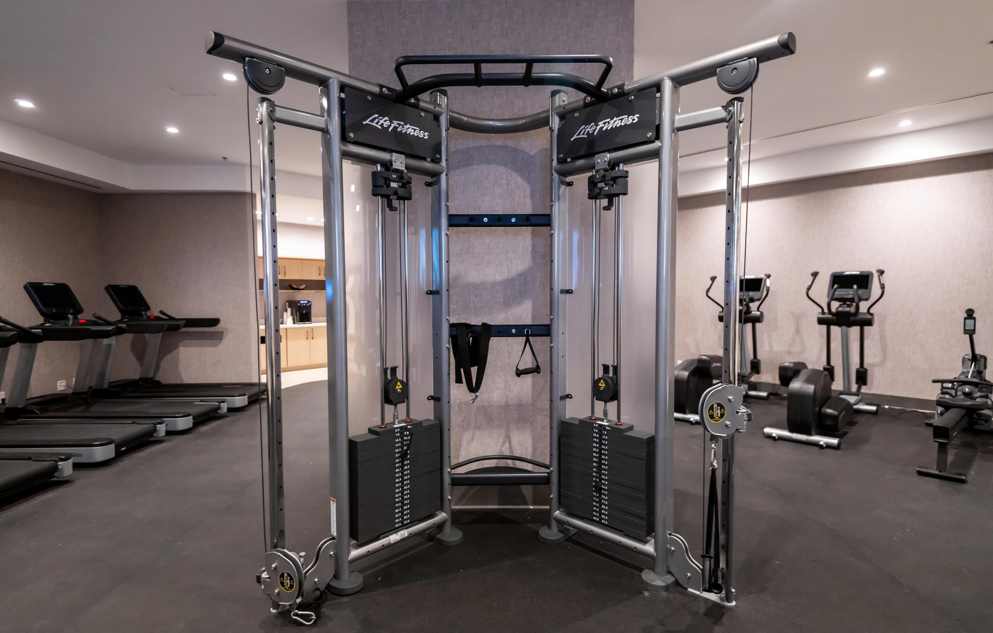 Un gimnasio con una máquina de cable central, cintas de correr y diversos equipos de ejercicio.