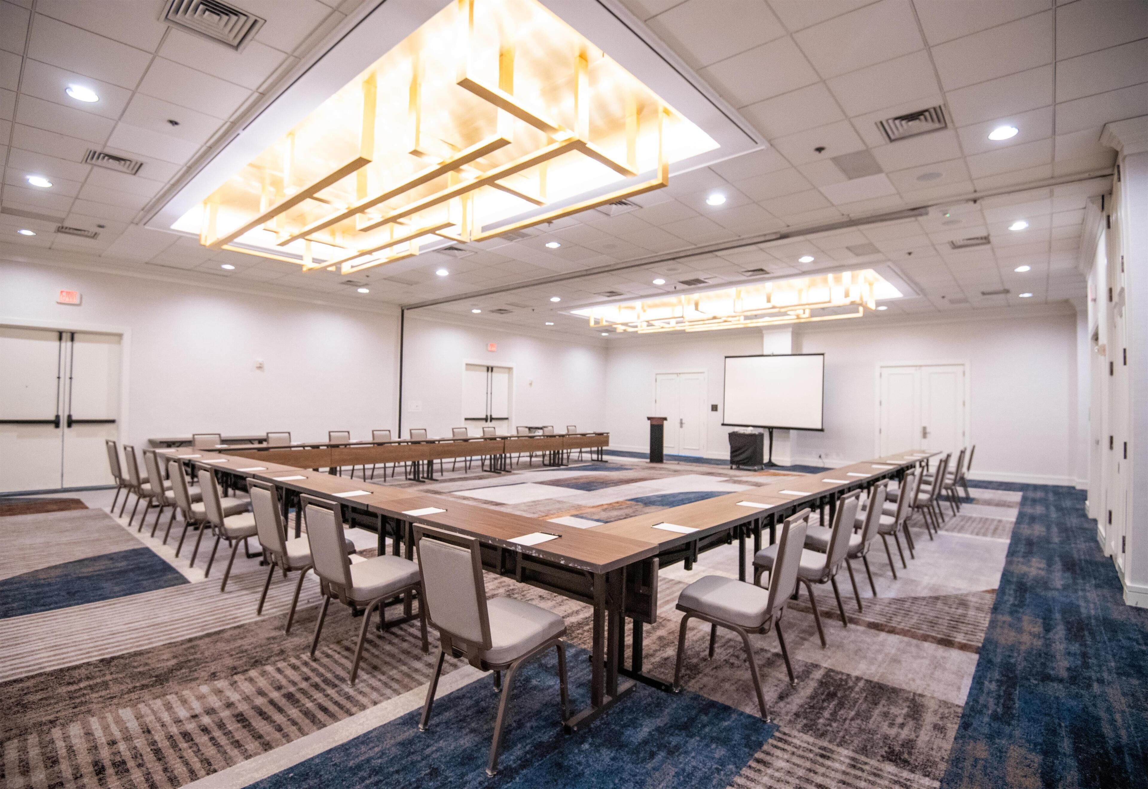 A conference room with a long table, chairs, a projector screen, and a carpeted floor.