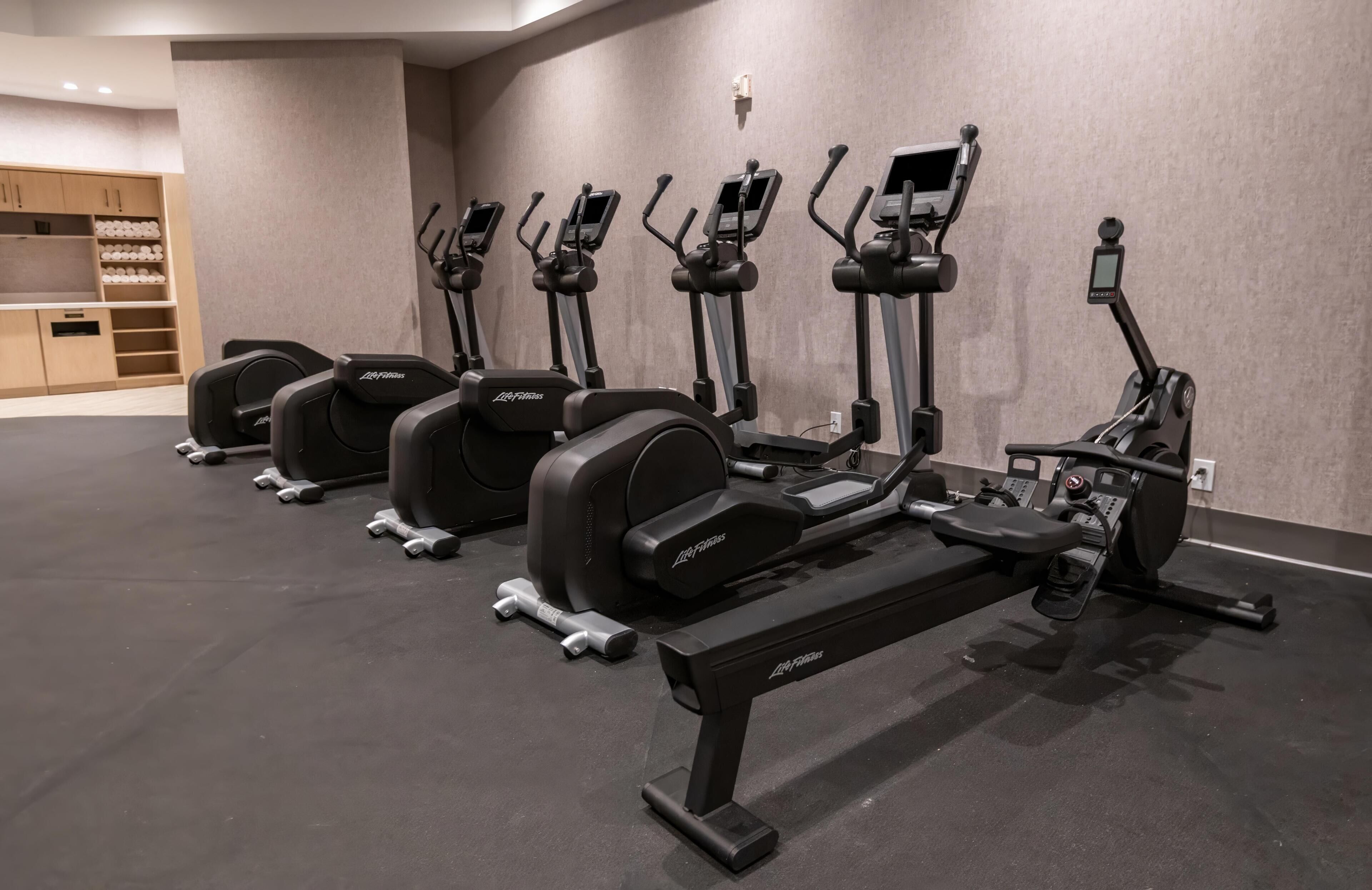 A gym with multiple elliptical machines, a bench, and dumbbells.