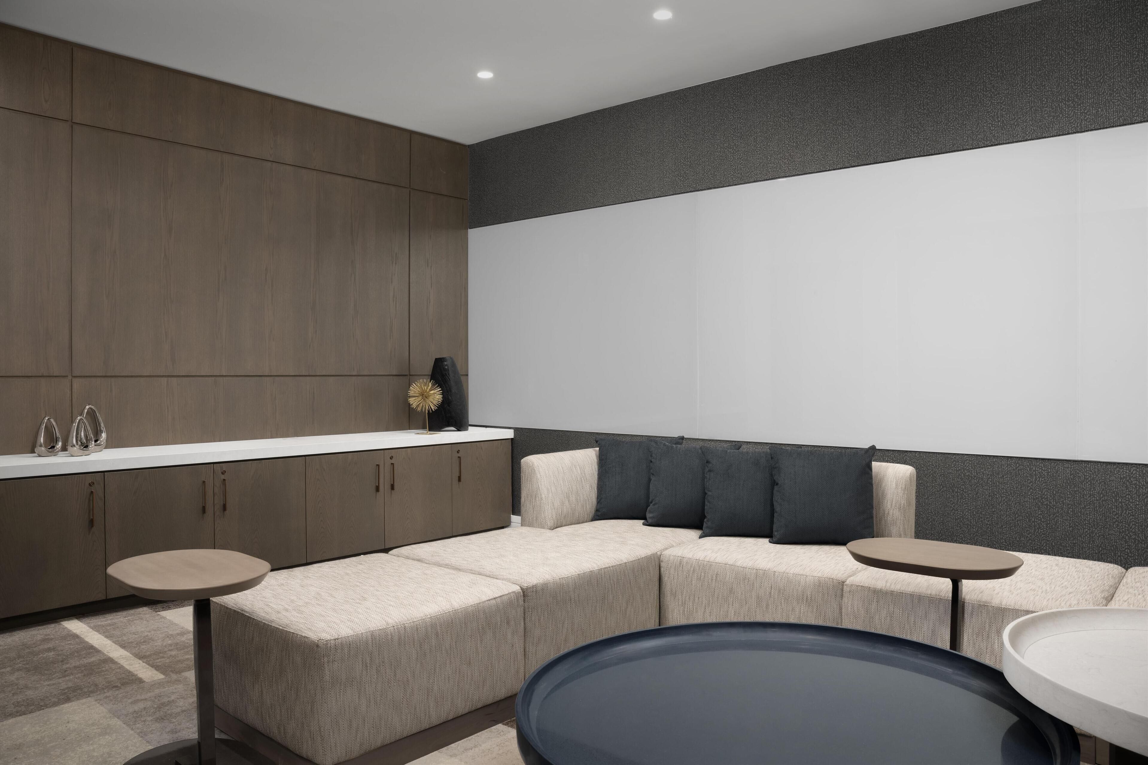 A modern living room with a sectional sofa, a round coffee table, and a kitchen area with cabinets and a countertop.
