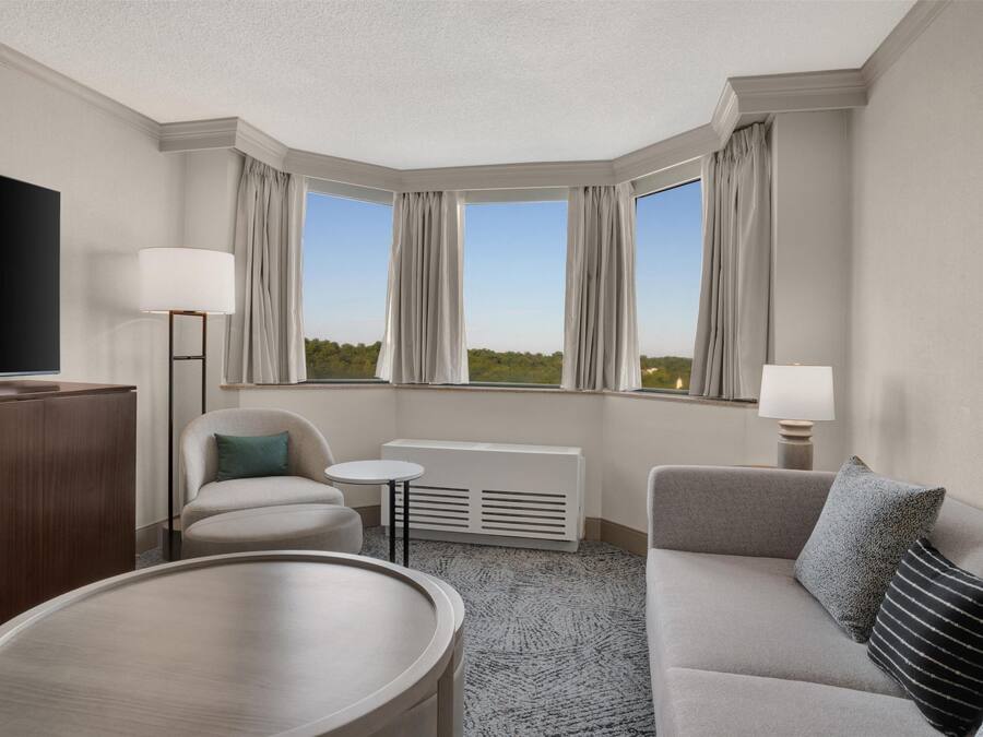A hotel room with a large window, a flat-screen TV, a sofa, a small table, and a radiator.