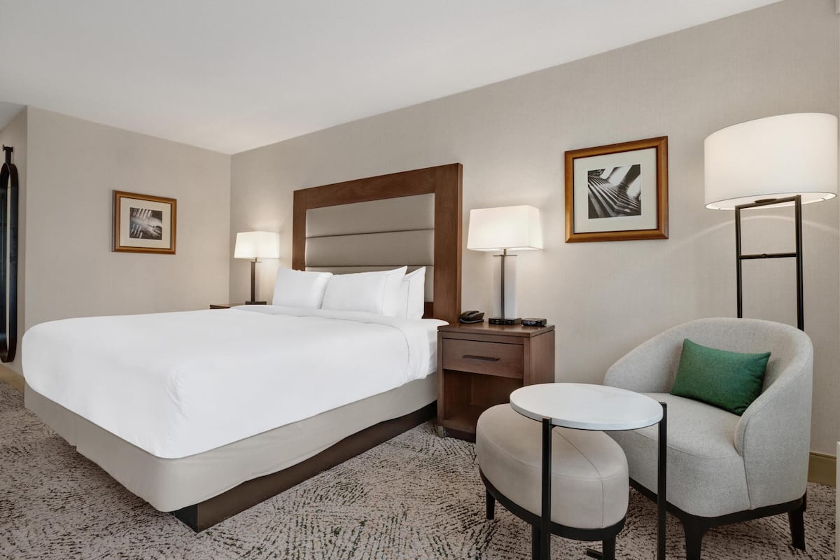 Habitación de hotel con una cama grande, una mesita de noche, una silla y dos lámparas fijadas a la pared.