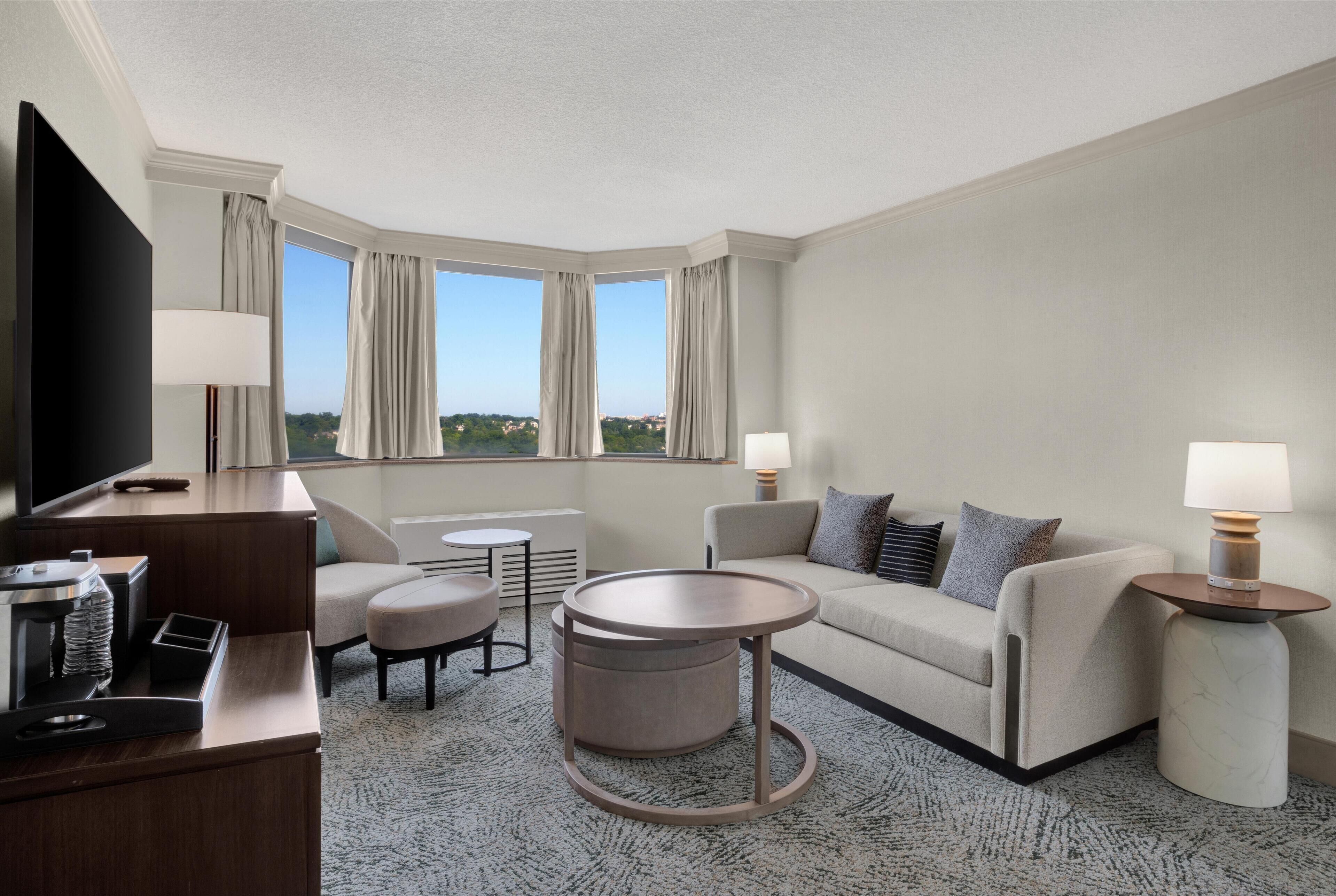 Ein modernes Hotelzimmer mit Flachbildfernseher, einer Couch, einem runden Couchtisch, einem kleinen runden Tisch und einer Lampe.