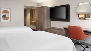 Quarto de hotel com duas camas, uma mesa, uma cadeira, uma televisão e um espelho.