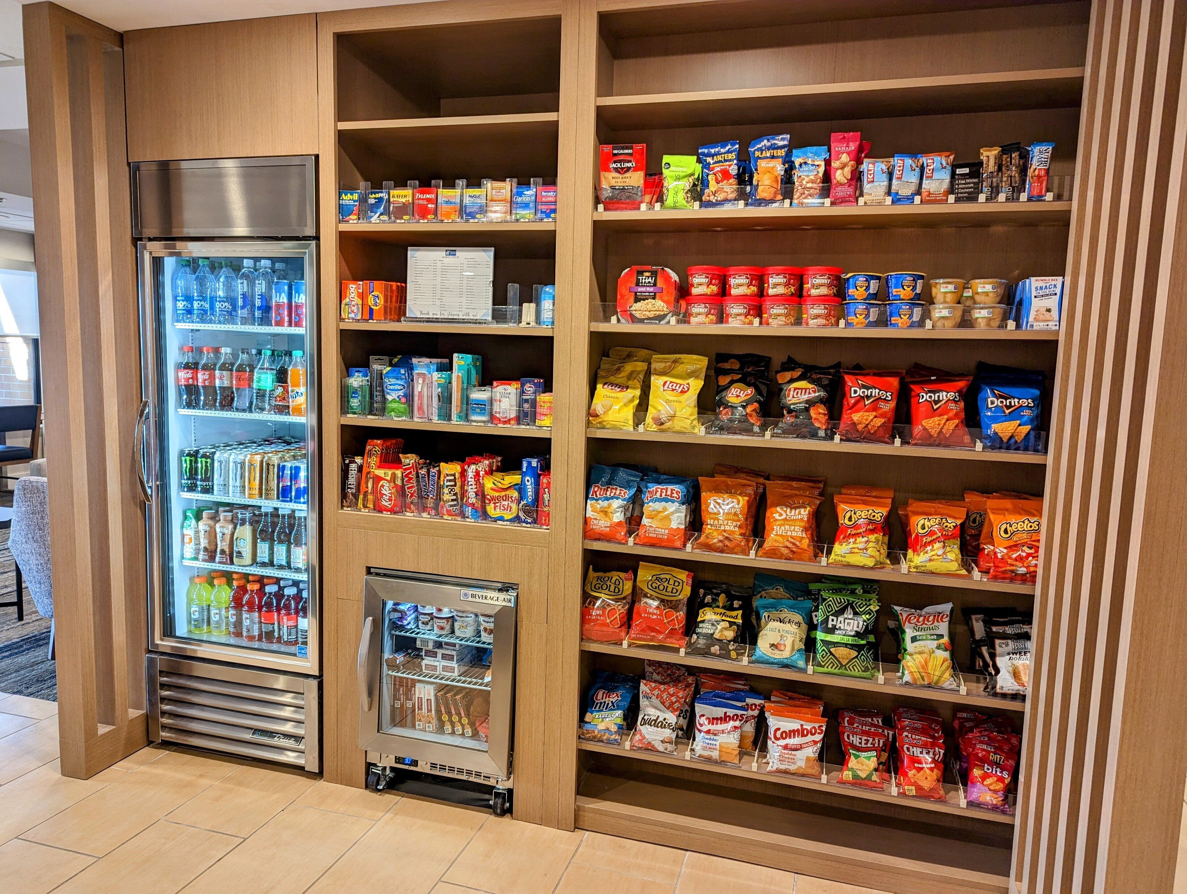 En försäljningsautomat fylld med snacks och drycker, inklusive märken som Lay’s, Doritos och Cheetos, placerad i en väl upplyst inomhusmiljö.