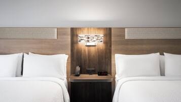 Habitación de hotel con dos camas, una mesita de noche con un reloj y una lámpara fijada en la pared.