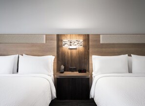 Une chambre d’hôtel avec deux lits, une table de chevet avec une horloge et un luminaire fixé au mur.