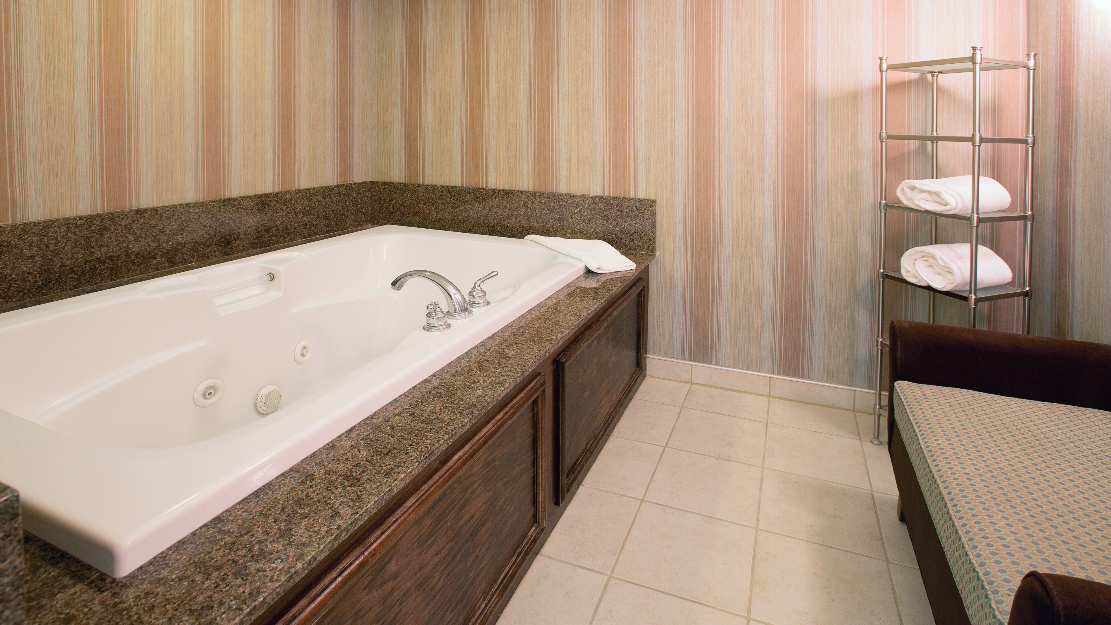 A bathroom with a large bathtub, a towel rack with towels, and a wooden vanity.