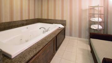 A bathroom with a large bathtub, a towel rack with towels, and a wooden vanity.