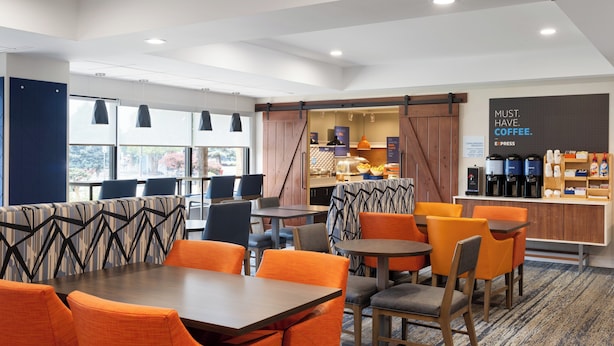 Um hall de hotel moderno com assentos laranja e cinza, um café e vista para o exterior.