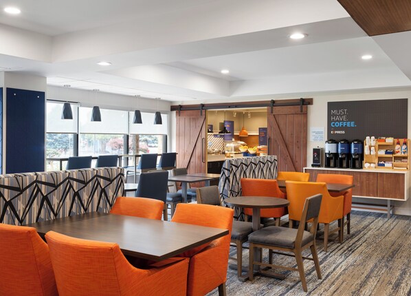 Un moderno vestíbulo de hotel con asientos naranja y gris, una cafetería y vistas al exterior.