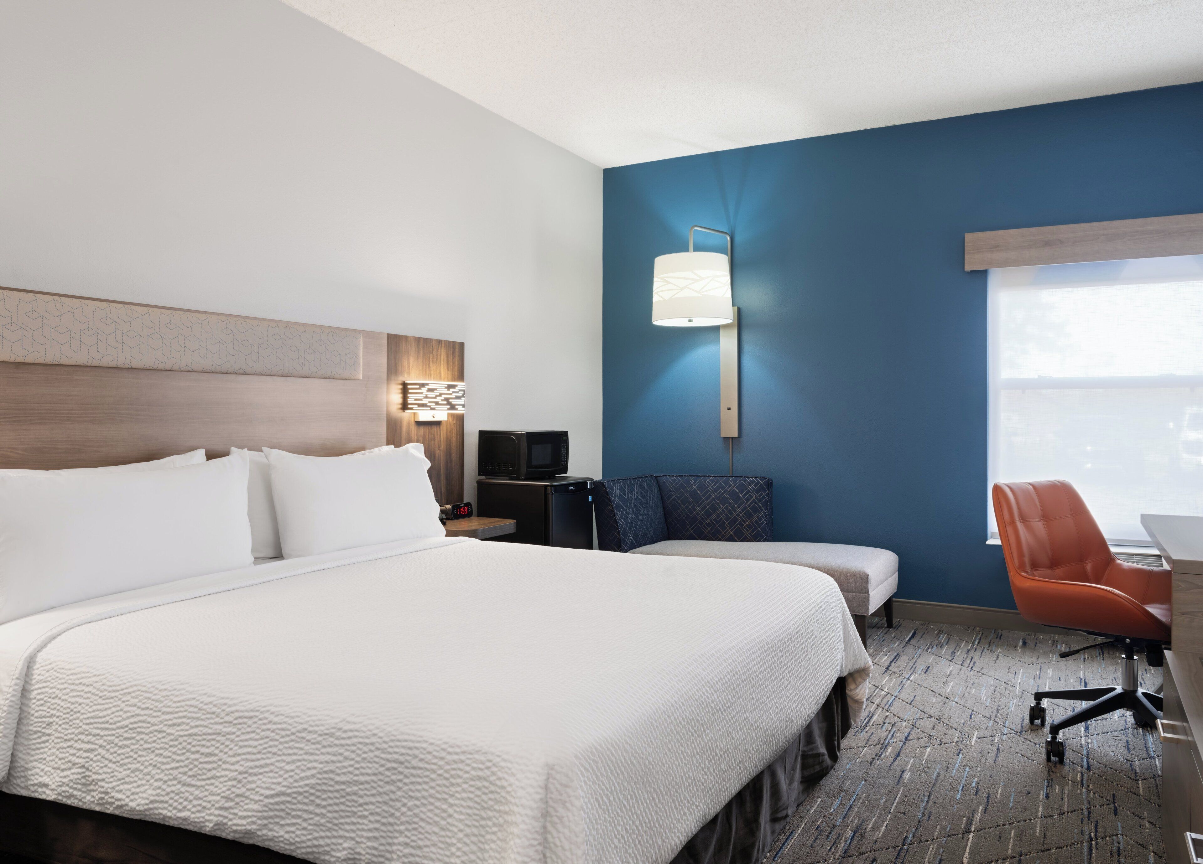 Ein Hotelzimmer mit einem großen Bett, einem Schreibtisch mit Stuhl, einer Mikrowelle und einem Nachttisch mit Lampe.