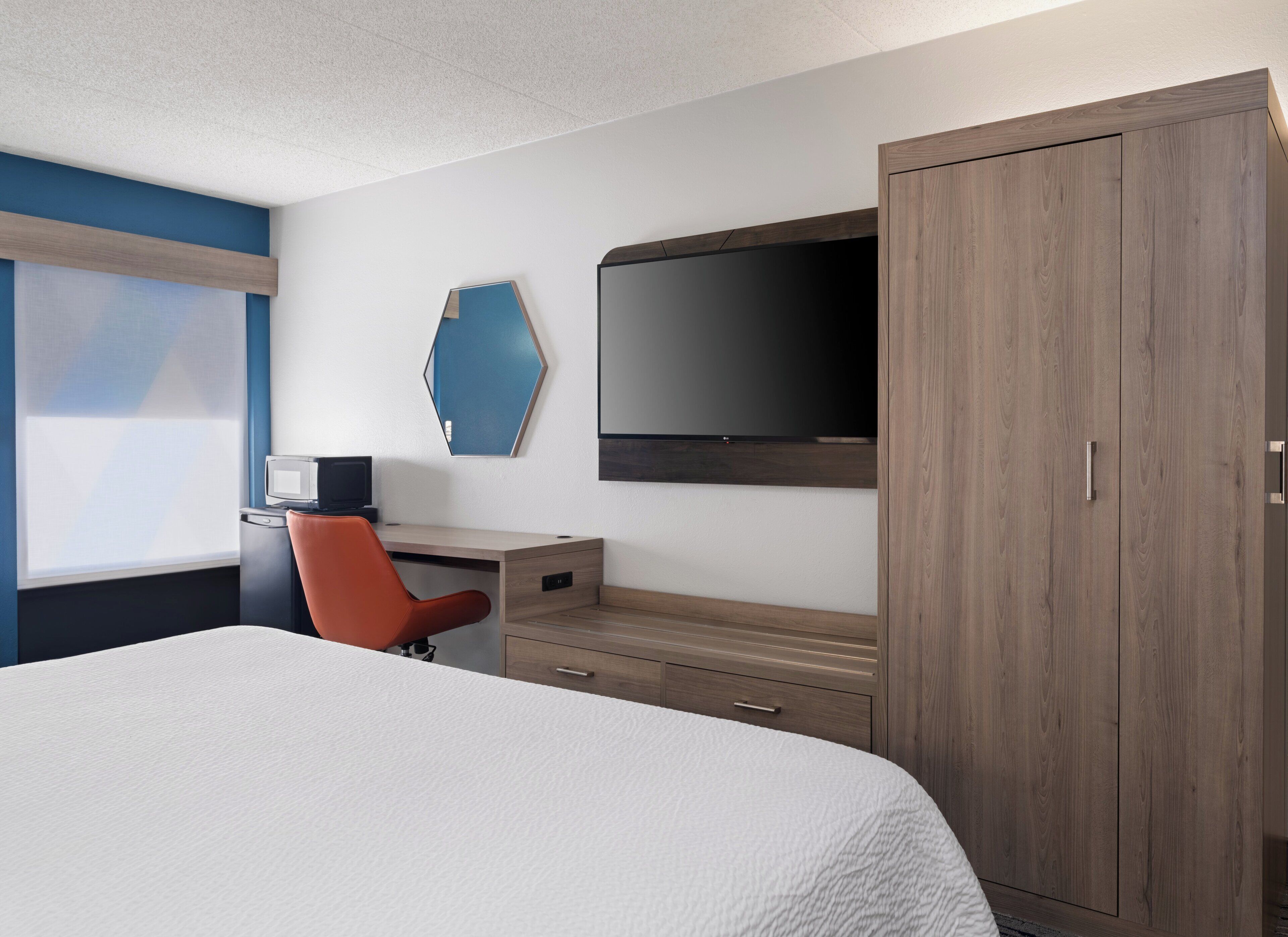 Una habitación de hotel con cama, escritorio con silla, televisión y armario.