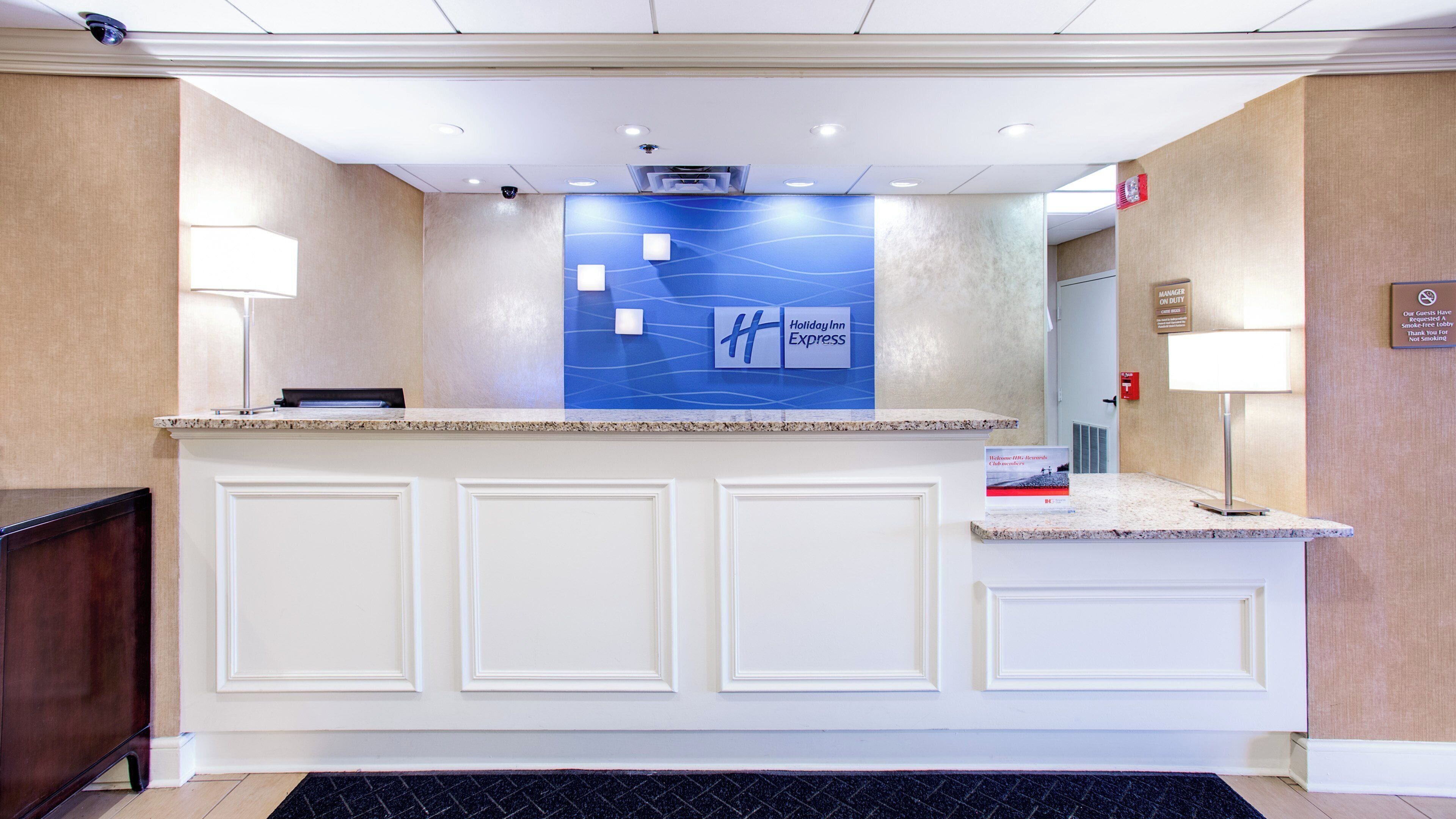 A hotel reception desk with a blue wall, a Holiday Inn Express sign, and a smoke-free lobby notice.