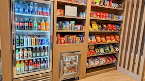 Máquina de bebidas automática com diversas opções de bebidas e uma prateleira com vários snacks de diferentes marcas.